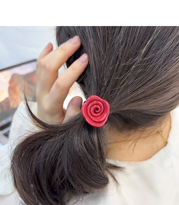 Nahaufnahme eines roten Acetat-Rosen-Haargummis auf dunklem Haar mit schwarzem Elastikband