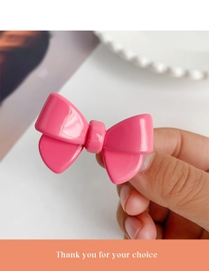 Detailed close-up of a sweet pink acetate bow hair clip held to show its compact size