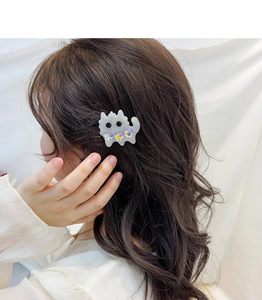 Detail of cute white cat hair clip with sparkling heart rhinestones on brunette wavy hair
