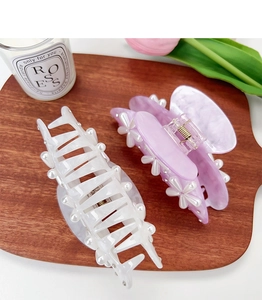 Detail of elegant acrylic hair clips with pearl flowers and marble patterns on wooden tray