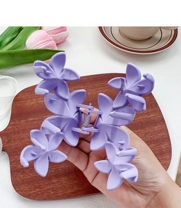 Détail d'une grande pince à cheveux fleurie violette mate tenue sur un plateau en bois