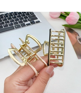 Handheld view of elegant gold metal hair claws with cream and black hollow rectangular designs