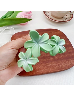 Détail de trois pinces à cheveux fleurs de frangipanier vert mat tenues à la main pour l'été
