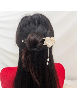Detail of elegant peony hair pin with gold chain and pearls worn on a dark hair bun