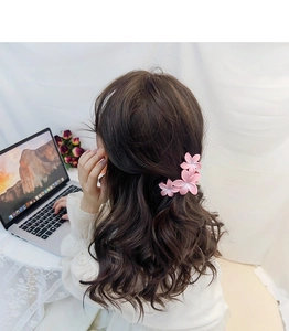 Pince à cheveux fleurie rose dégradé portée sur de longs cheveux bruns ondulés