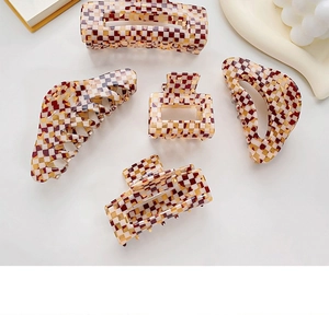 Flat lay of five checkered acetate hair claws in brown and beige tones with a white candle