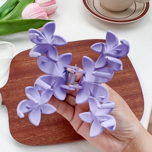 Grande pince à cheveux fleur mauve mate tenue à la main dans un cadre de vie doux