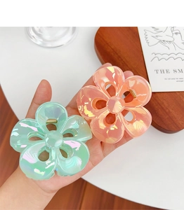 Macro detail of large iridescent hollow plumeria hair claws in mint green and peach pink