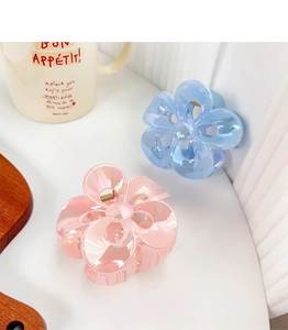 Detail of pink and light blue plumeria flower claw clips with golden springs on a white table