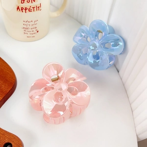 Iridescent flower-shaped hair clips in pink and blue colors on a wooden tray
