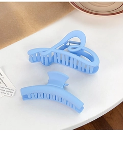 Detail view of light blue matte heart-shaped and curved hair claws on a clean desk