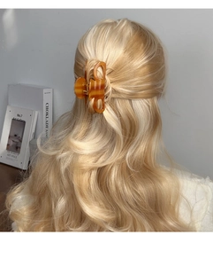 Gros plan d'une pince à cheveux en acétate ambre portée sur de longs cheveux ondulés