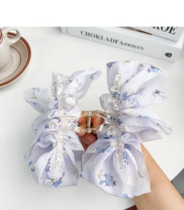 Detail of a large light blue floral bow hair claw clip held over a cozy coffee scene