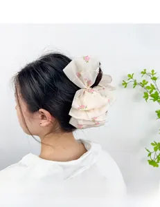 Detailed embroidery of pink roses on white organza bow hair clip worn by a model
