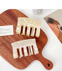 Detail of acetate square hair claws in marble and pearlescent finishes on wooden tray