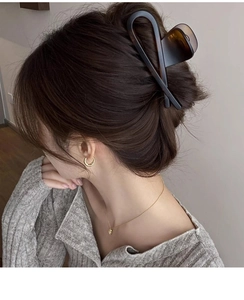 Détail d'une grande pince à cheveux mate marron foncé portée sur les cheveux d'une femme