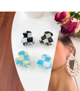 Close-up of four checkered small hair clips in black, blue and white on a white tray