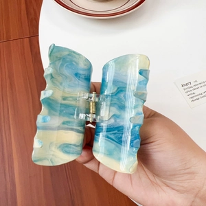 Large marble acrylic hair claw clip with blue and gold accents in hand-held display