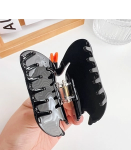 Detail of a large black butterfly hair claw clip with orange accents and a gold metal spring