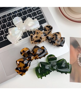 Detailed collection of acetate bow hair claws in white pearl, tortoiseshell, and green