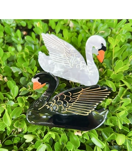 Detailed close-up of elegant black and white swan acetate hair claws on green leaves
