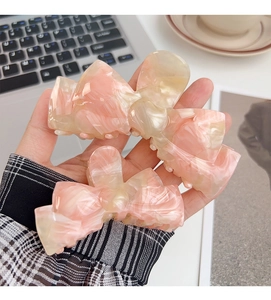 Detailed view of pink and cream marble acetate bow hair claws in two sizes
