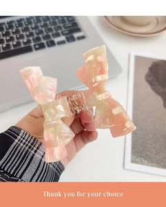 Detailed close-up of marble pattern acetate bow hair claw clip with golden metal spring