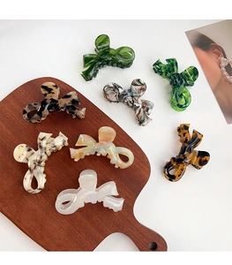 Flat lay of eight colorful acetate bow hair claws on a wooden tray with marble patterns