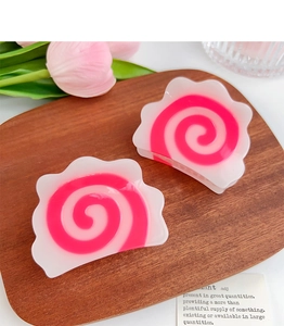 Close-up of Narutomaki style hair clips with pink spiral patterns on a wooden tray