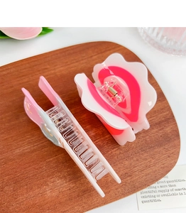 Close-up of pink petal-shaped acetate hair claws on a wooden tray with soft lighting