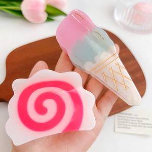 Pink and pastel acetate ice cream and spiral hair claw clips held by hand in home setting