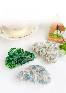 Detailed view of three acetate leaf hair claws in green, marble, and floral textures