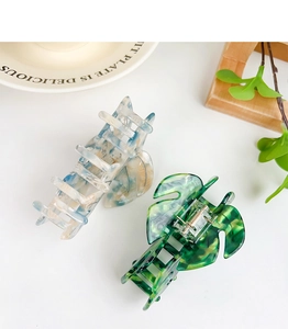 Detailed view of large acetate claw clips in blue marble and green monstera leaf designs