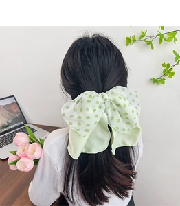 Detail view of a large green polka dot bow hair scrunchie worn by a model in a cozy setting