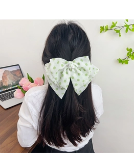 Detail of white and green polka dot bow hair clip with pearl on dark straight hair