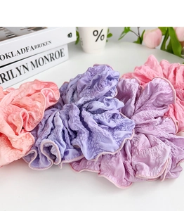 Close-up of pastel pink and purple oversized pleated fabric scrunchies on a white table