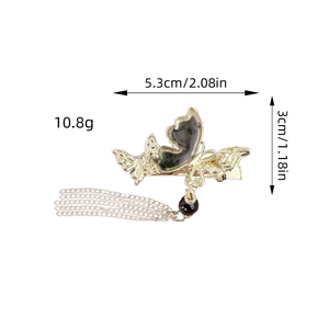 Pince à cheveux papillon dorée avec chaîne à pompons et perle foncée sur fond blanc