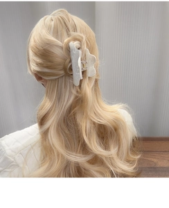 Détail d'une pince à cheveux en acrylique marbré blanc sur des cheveux blonds ondulés