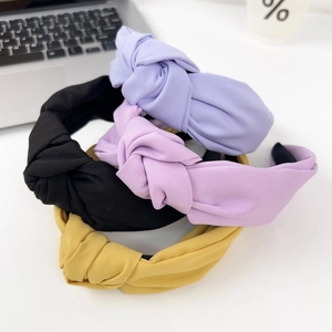 Minimalist wide knot headbands in black, blue, and yellow on a desk with accessories