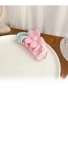 Macro detail of large floral hair claw clip with pink and blue gradient on a white plate