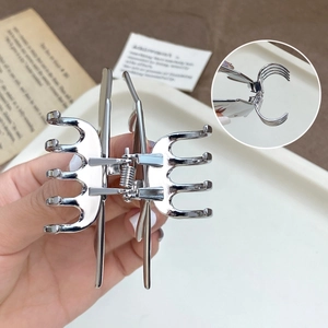 Bat-shaped silver metal hair claw clip with hollow design shown in hand for grip size