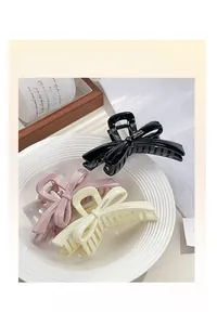 Detailed view of glossy resin bow hair claws in black, pink, and cream on a ceramic plate