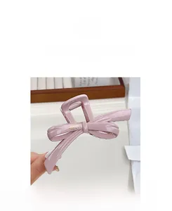 Detail shot of a pink glossy bow hair claw clip featuring golden brand lettering on the side