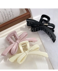 Three elegant bow hair clips in black, pink, and cream white displayed on a tray