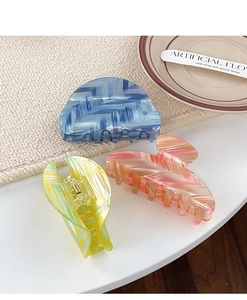 Three large striped hair claws in blue, pink, and green on a stylish ceramic plate