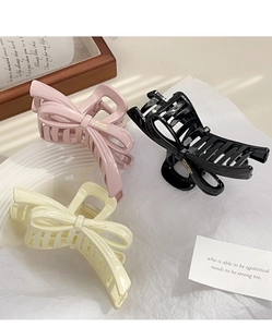 Three elegant bow hair claws in pink, black, and cream yellow shown on a decorative background
