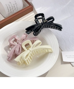 Close-up of three glossy bow hair claws in black, pink, and cream on a ceramic tray