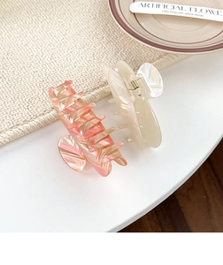 Detail view of two large pearlescent hair claws in pink marble and cream white finish