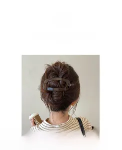 Detail of a large oval dark brown resin hair clip securing a hair bun in a lifestyle setting