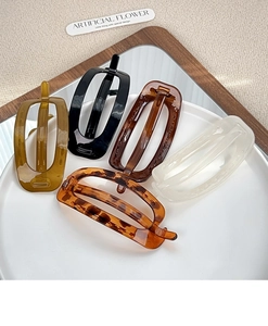Detail view of five oval resin hair clips in neutral colors on a white ceramic plate